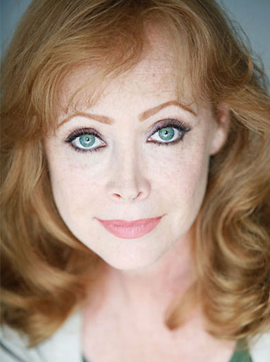 Portrait of a woman with wavy red hair and striking green eyes. Her soft expression conveys warmth and approachability, suitable for a professional profile.